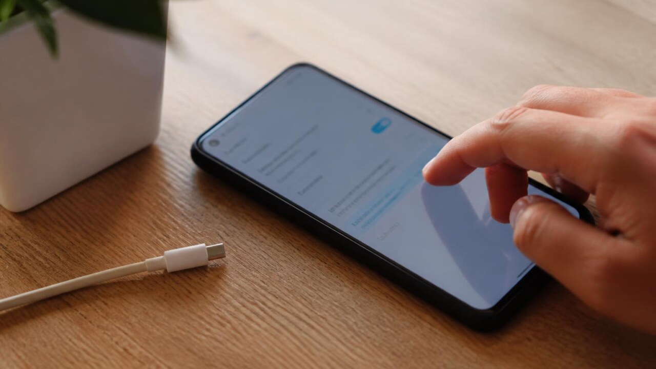 Pessoa verificando atualizações em um smartphone sobre uma mesa com cabo de carregador ao lado