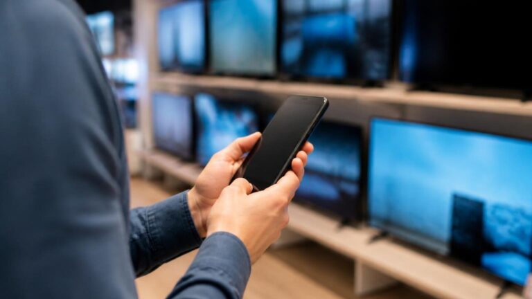 Pessoa segurando um celular em mãos, comparando telas de diferentes modelos em loja