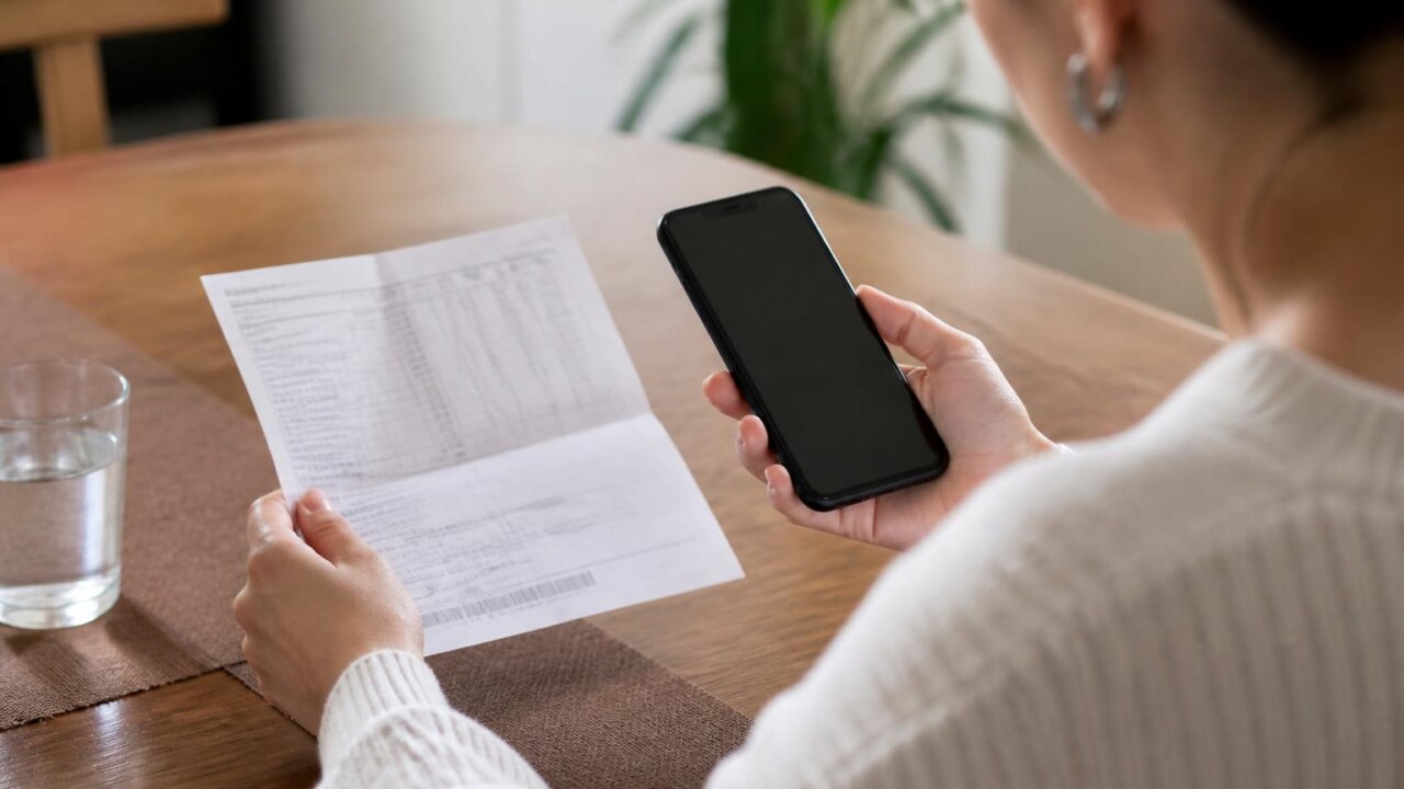 Pessoa conferindo fatura e celular para identificar assinaturas de aplicativos