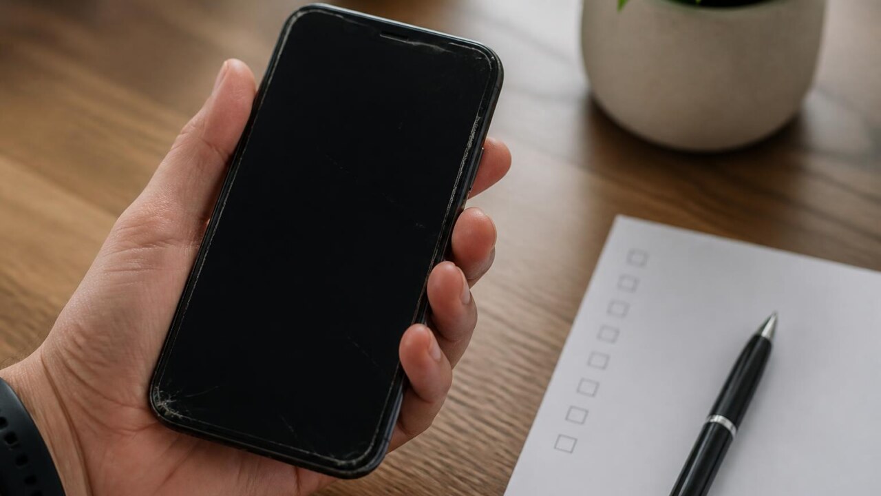 Pessoa examinando um smartphone usado com uma lista de verificação ao lado