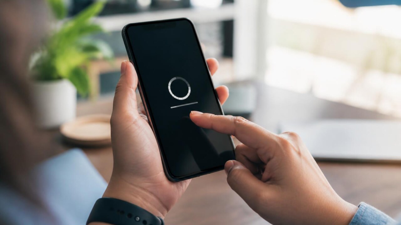 Pessoa segurando um smartphone com tela de atualização de sistema, em ambiente doméstico bem iluminado.