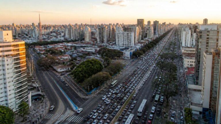 Vista aérea de uma cidade com congestionamento em horário de pico e vias laterais com trânsito mais fluido